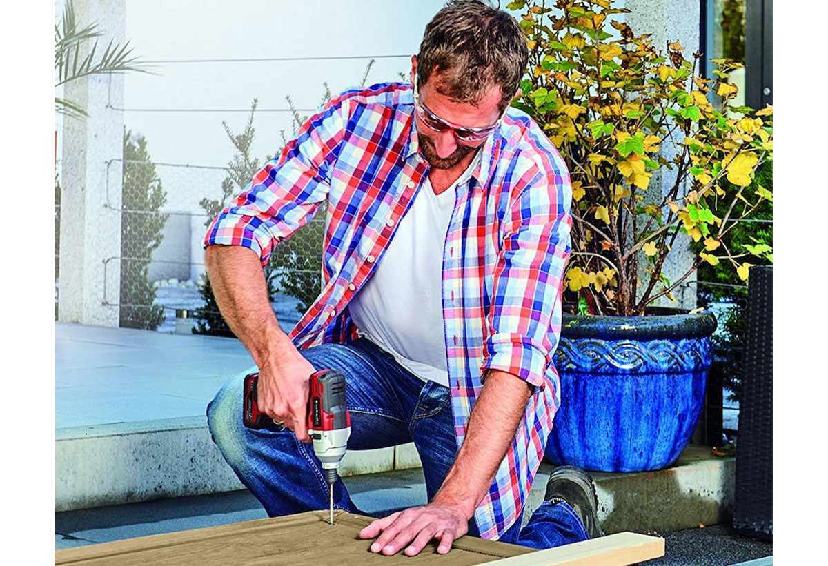 Απεικονίζεται ένας άνδρας να τρυπάει μια ξύλινη επιφάνεια με το κατσαβίδι.